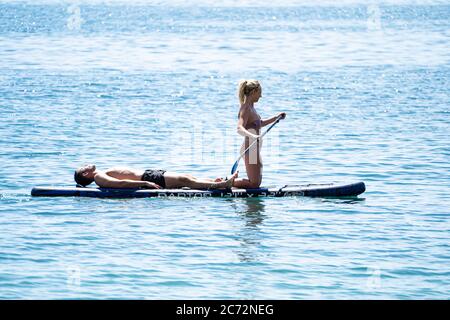 A young couple, man and woman, on a SUP (Stand up paddleboard), the man lying down (asleep?) and the woman kneeling and gently paddling, Dorset, UK Stock Photo
