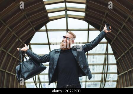 Stylishly dressed young man with a beard learns the good stunning news by phone. Lifestyle emotional city portrait Stock Photo