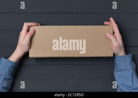 Craft paper box in children's hands on black background. Top view. Copy space Stock Photo