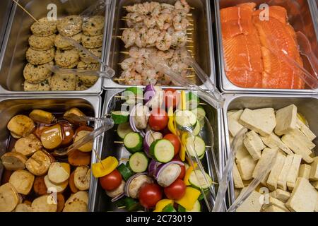Variety of fresh skewers and meat products on the butcher display refrigerator in the Supermarket. salmon, shrimps, tofu and vegetarian patties in top view. Stock Photo