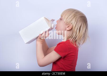 fair-haired boy drinking milk or juice from large carton. Portrait of child with carton of milk on white background. Stock Photo