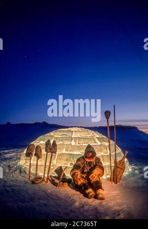 Inuit man and tools silhouetted  against a lit igloo at dusk outside Baker Lake, Nunavut. Stock Photo