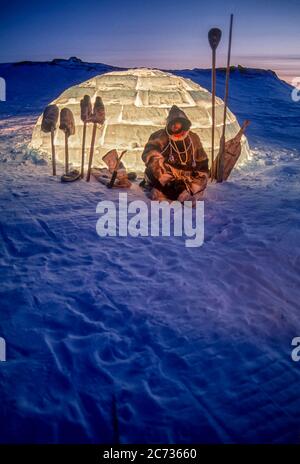 Inuit man and tools silhouetted  against a lit igloo at dusk outside Baker Lake, Nunavut. Stock Photo