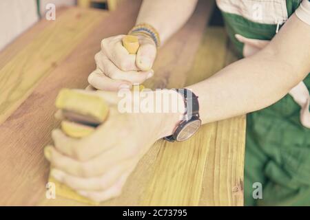 Carpenter working with plane on table in his workshop. Carpenter working with plane in a carpentry shop. Young carpenter wearing bracelets Stock Photo