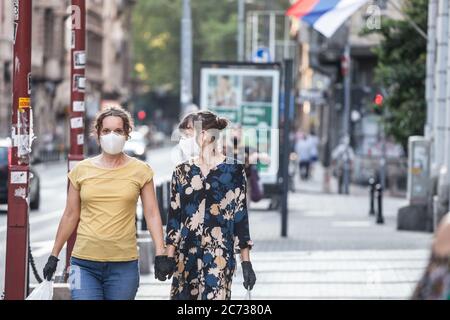 BELGRADE, SERBIA - JUNE 6, 2020: Young people, two young women friends, walking holding hands wearing face mask protective equipement and latext glove Stock Photo