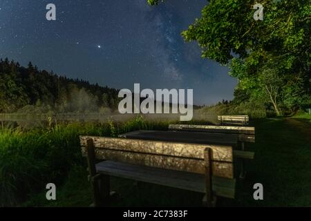 Focused milkyway at a star clear night in southern bavaria with a blurry park bench in foreground, idyllic moment in the night. Stock Photo