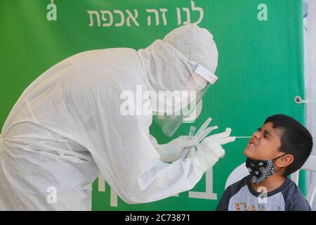 Lod, Israel. 13th July, 2020. A medical worker collects a swab from a boy for a COVID-19 test in Lod, central Israel, on July 13, 2020. Israel's Ministry of Health has reported 1,962 new coronavirus cases on Monday, bringing the total cases to 40,632. Credit: Gil Cohen Magen/Xinhua/Alamy Live News Stock Photo