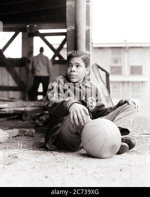 1960s BORED DEJECTED TEENAGE AFRICAN AMERICAN BOY SITTING IN DERELICT CITY PLAYGROUND WITH HIS DEFLATED BASKETBALL - n1944 HAR001 HARS FITNESS JUVENILE FACIAL ANGER FEAR HEALTHY SAFETY ATHLETE LIFESTYLE POOR HEALTHINESS HOME LIFE COPY SPACE FULL-LENGTH PERSONS INSPIRATION CARING MALES RISK TEENAGE BOY ATHLETIC CONFIDENCE EXPRESSIONS B&W SADNESS TEMPTATION ACTIVITY DREAMS PHYSICAL HIS STRENGTH AFRICAN-AMERICANS AFRICAN-AMERICAN EXTERIOR POWERFUL RECREATION BLACK ETHNICITY DIRECTION PRIDE FEELING CONCEPTUAL ESCAPE FLEXIBILITY MUSCLES TEENAGED DISADVANTAGED DEJECTED DISAFFECTED DISAPPOINTED Stock Photo