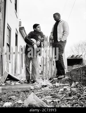 1960s TWO AFRICAN AMERICAN TEENAGE BOYS HOLDING BASKETBALL IN POVERTY STRICKEN URBAN NEIGHBORHOOD PHILADELPHIA PA USA  - n1962 HAR001 HARS JUVENILE ANGER FEAR BALANCE SAFETY COMPETITION LIFESTYLE BROTHERS POOR HEALTHINESS HOME LIFE UNITED STATES COPY SPACE FRIENDSHIP FULL-LENGTH UNITED STATES OF AMERICA MALES RISK TEENAGE BOY SIBLINGS B&W SADNESS NORTH AMERICA FREEDOM NORTH AMERICAN TEMPTATION DREAMS WELLNESS NEIGHBORHOOD STRATEGY AFRICAN-AMERICANS COURAGE AFRICAN-AMERICAN LOW ANGLE PA POWERFUL BLACK ETHNICITY PRIDE IN OF ON OPPORTUNITY SIBLING CONCEPTUAL ESCAPE DISADVANTAGED DISAFFECTED Stock Photo