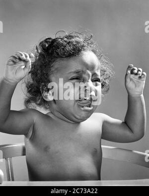 1940s 1950s EXTREMELY UNHAPPY CRYING AFRICAN AMERICAN BABY GIRL ARMS RAISED IN PROTEST SITTING IN HIGH CHAIR VERY UPSET - n326 HAR001 HARS HALF-LENGTH B&W SADNESS VERY HEAD AND SHOULDERS STRENGTH AFRICAN-AMERICANS AFRICAN-AMERICAN COMPOSITE EXCITEMENT LOUD POWERFUL BLACK ETHNICITY IN EXTREMELY PROTESTING JUVENILES BLACK AND WHITE HAR001 OLD FASHIONED AFRICAN AMERICANS Stock Photo