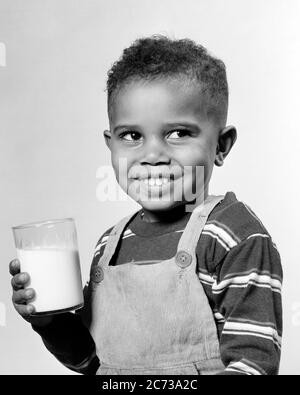 1940s 1950s SMILING AFRICAN-AMERICAN BOY HOLDING DRINKING GLASS OF MILK WEARING BIB OVERALL STRIPED T-SHIRT LOOKING OFF TO SIDE - n628 HAR001 HARS SATISFACTION STRIPED STUDIO SHOT HEALTHINESS HOME LIFE DAIRY COPY SPACE HALF-LENGTH MALES CONFIDENCE EXPRESSIONS B&W HAPPINESS CHEERFUL BEVERAGE AFRICAN-AMERICANS AFRICAN-AMERICAN AND EXCITEMENT FLUID BLACK ETHNICITY OF TO SMILES CONNECTION CONSUME CONSUMING HYDRATION JOYFUL OVERALL T-SHIRT BIB GROWTH JUVENILES PROTEIN REFRESHING BEVERAGES BLACK AND WHITE HAR001 OLD FASHIONED AFRICAN AMERICANS Stock Photo
