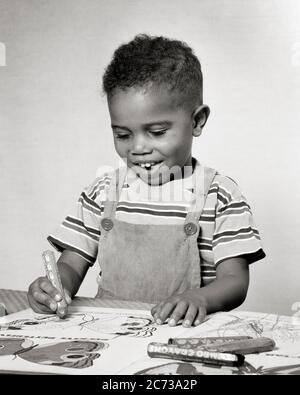 1940s 1950s CREATIVE SMILING AFRICAN-AMERICAN BOY TODDLER SITTING AT TABLE WORKING DRAWING IN COLORING BOOK WITH FAT CRAYONS - n641 HAR001 HARS COMMUNICATION LAUGH PLEASED JOY LIFESTYLE HEALTHINESS HOME LIFE COPY SPACE HALF-LENGTH MALES CONFIDENCE EXPRESSIONS B&W GOALS SUCCESS HAPPINESS WELLNESS CHEERFUL DISCOVERY STRENGTH AFRICAN-AMERICANS AFRICAN-AMERICAN HOPE CHOICE CREATIVE EXCITEMENT RECREATION BLACK ETHNICITY DIRECTION PRIDE AT IN OPPORTUNITY SMILES CRAYONS CONCEPTUAL JOYFUL STYLISH PROMISE GROWTH JUVENILES BLACK AND WHITE COLORING HAR001 OLD FASHIONED AFRICAN AMERICANS Stock Photo