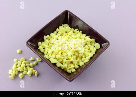 Mini white chocolate chips in purple ingredient bowl on lavender background Stock Photo
