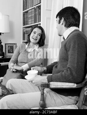 1970s COUPLE IN LIVING ROOM LAUGHING WOMAN SITTING WITH HANDS CLASPED FINGERS INTERTWINED LOOKING AT MAN HOLDING CUP AND SAUCER - s20812 HAR001 HARS PAIR ROMANCE FLIRTING OLD TIME NOSTALGIA OLD FASHION 1 COMMUNICATION LAUGH BALANCE TEAMWORK FINGERS PLEASED JOY LIFESTYLE FEMALES MARRIED SPOUSE HUSBANDS HOME LIFE COPY SPACE FRIENDSHIP HALF-LENGTH LADIES PERSONS CARING MALES NERVOUS B&W PARTNER DATING HAPPINESS CHEERFUL STRATEGY AND EXCITEMENT AT IN OPPORTUNITY SMILES CONNECTION CLASPED JOYFUL MID-ADULT MID-ADULT MAN MID-ADULT WOMAN RELAXATION TOGETHERNESS WIVES BLACK AND WHITE Stock Photo