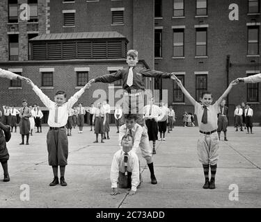 1930s GROUP OF ANONYMOUS PRETEEN BOYS IN SCHOOL YARD ALL LOOKING AT CAMERA WEARING KNICKERS PERFORMING EXERCISE CALISTHENICS  - s6886 HAR001 HARS JUVENILE YARD ELEMENTARY FACIAL STYLE HEALTHY BALANCE COMIC PUBLIC TEAMWORK ATHLETE KNICKERS PLEASED JOY LIFESTYLE CELEBRATION HEALTHINESS COPY SPACE FULL-LENGTH MALES RISK ALL ATHLETIC CONFIDENCE EXPRESSIONS B&W EYE CONTACT PERFORMING SCHOOLS SUCCESS WIDE ANGLE ACTIVITY GRADE HUMOROUS PHYSICAL WELLNESS CHEERFUL STRENGTH EXCITEMENT RECREATION COMICAL PRIDE IN OF PRETEEN PRIMARY SMILES CONCEPTUAL CALISTHENICS COMEDY FLEXIBILITY JOYFUL MUSCLES STYLISH Stock Photo