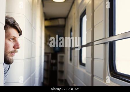 Handsome young caucasian man with a beard, looks outside of the train's window Stock Photo