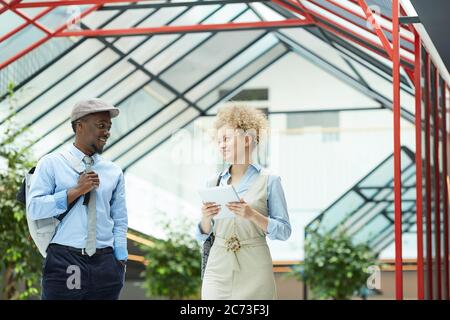Young businesswoman using digital tablet and smiling to her colleague while they standing and talking at office hall Stock Photo
