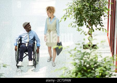 Young businesswoman talking to her disabled colleague in wheelchair at the office corridor Stock Photo