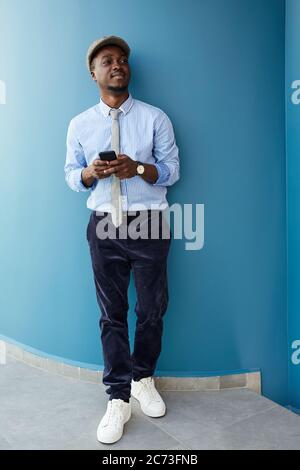 African young businessman leaning on the blue wall and using his mobile phone Stock Photo