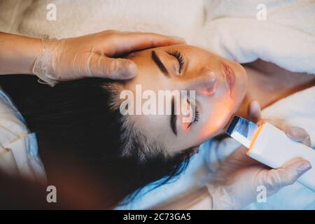 Facial skin procedure done with a special apparatus to a brunette lady lying on spa couch Stock Photo