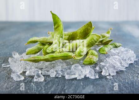 Frozen Edamame or soybeans in the mix with crushed ice on a blue background. Stock Photo