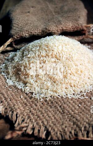Rice out from small sack isolated on wooden background. Fresh rice in sack bag over wooden textured background. Close up raw rice grain on sack cloth. Stock Photo