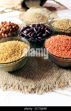 Rice out from small sack isolated on white background. Different colorful pulse in bowls. Chick Pea, Red Kidney, Lentil, Fenugreek Seed, Wheat Dalia,