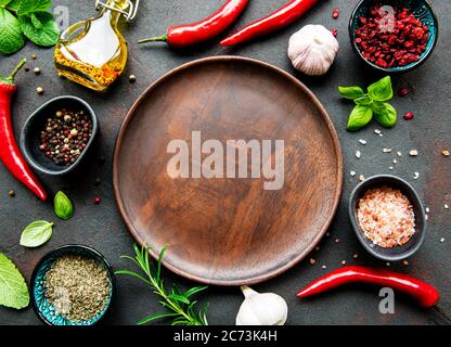 Empty wooden plate and frame of spices, herbs and vegetables on a dark stone background. Top view, flat lay. Stock Photo