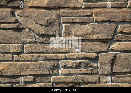 Beige-colored decorative stone wall, texture, background. Tan or light-brown stones of irregular shape in the wall construction. Decorative stones Stock Photo