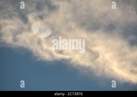The Moon is Rising in a Blue Sky With white wispy Clouds in the Foreground Stock Photo