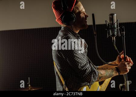 young caucasian professional guitarist singing on microphone and playing guitar contemporaneously. music, rock and roll concept Stock Photo