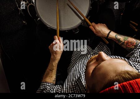 young caucasian drummer rehearsing on drums before rock concert. professional artiste man recording music on drum set in dark studio Stock Photo