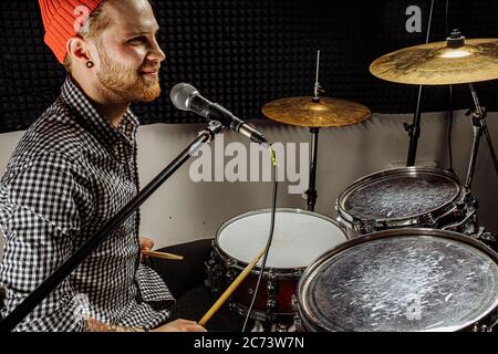 gorgeous talented caucasian singer play on drums and sing his favourite song, rocker man love his job, musician in recording studio, enjoy Stock Photo