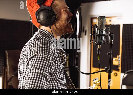 professional caucasian singer man sing in recording studio. handsome guy enjoy performing music, emotional singer with microphone and headset Stock Photo