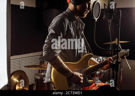 young caucasian gorgeous musician play electric guitar and sing on microphone in recording studio. rockstar perform music. man preparing, practicing b Stock Photo