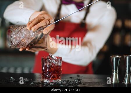 The bartender man pours ruby cocktail into crystal glass, close up, Barman is out of focus. Bar, Restaurant Beverage and Service concept. Stock Photo