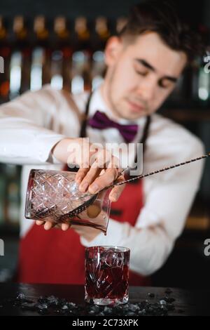 The bartender man pours ruby cocktail into crystal glass, close up. Bar, Restaurant Beverage and Service concept. Stock Photo