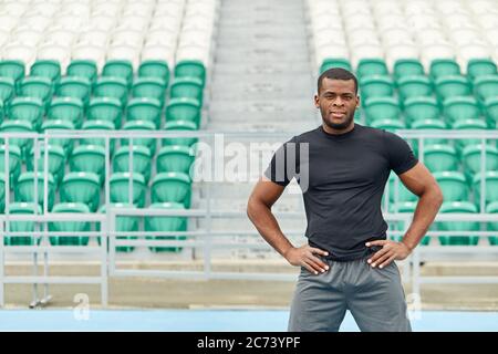 muscular strong handsome cheerful mixed race sportsman standing with hands on hips at the stadium. close up photo. resrtl. free time, spare time, trai Stock Photo