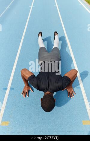 motivated african athletic young man doing push-ups at the stadium, full length back view photo. sport, health and body care, lifestyle. motivation, s Stock Photo