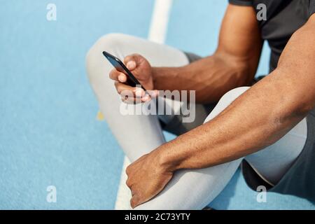 well-built muscular runner holding smart phone, surfing, browsing the net. close up cropped side view photo, technology, gadget Stock Photo
