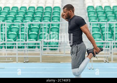 motivated strong man stetching his legs, warming up before training, side view close up portrait. green seats in the background of the photo.health, b Stock Photo