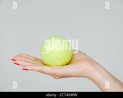 A Female Hand with Red Manicured Nails holds a green tennis ball Stock Photo