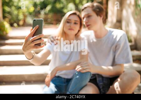 Young beautiful couple sitting and making selfie. Close up photo of woman hand holding mobile phone and taking photo on cellphone frontal camera Stock Photo