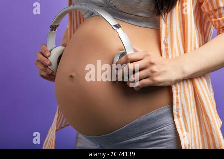 Young fun relaxed pregnant future mom woman with tummy wearing casual  clothes put headphones on belly for baby to listen to music isolated on  plain pastel blue background. Maternity pregnancy concept. Stock