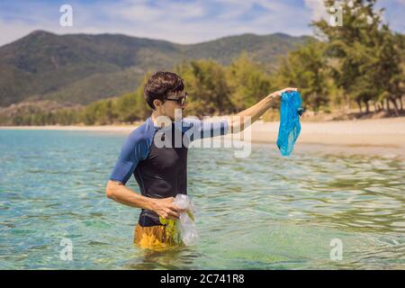 Man collects packages from the beautiful turquoise sea. Paradise beach pollution. Problem of spilled rubbish trash garbage on the beach sand caused by Stock Photo