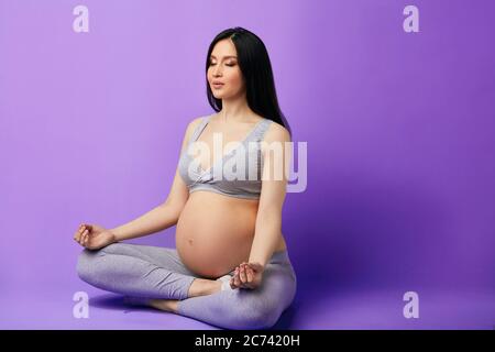 Pregnant woman with closed eyes meditating, sitting in lotus position, keeping fingers in mudra gesture. pregnancy, yoga, people and healthy lifestyle Stock Photo