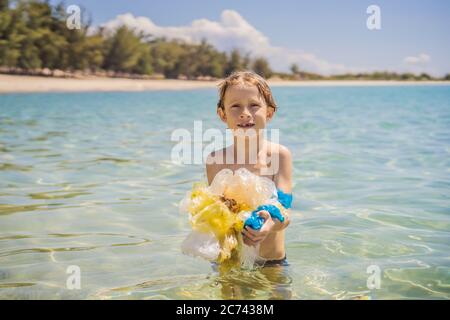Boy collects packages from the beautiful turquoise sea. Paradise beach pollution. Problem of spilled rubbish trash garbage on the beach sand caused by Stock Photo