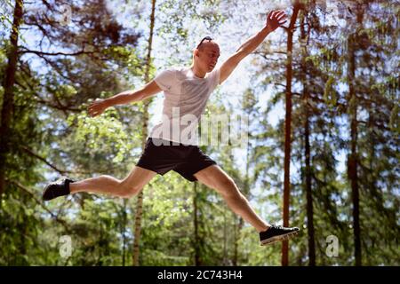 Young man jumps on a rock in a coniferous forest. Active extreme tourism.