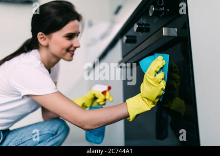 Beautiful woman in protective gloves cleaning oven with rag Stock Photo