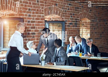 In the foreground two blonde caucasian women, caucasian bearded brunette man, african man discuss. On the background two blonde caucasian men and one Stock Photo